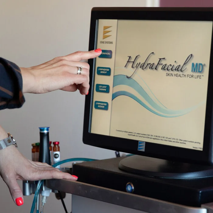 Frauenhände am Touchscreen mit HydraFacial™ Logo